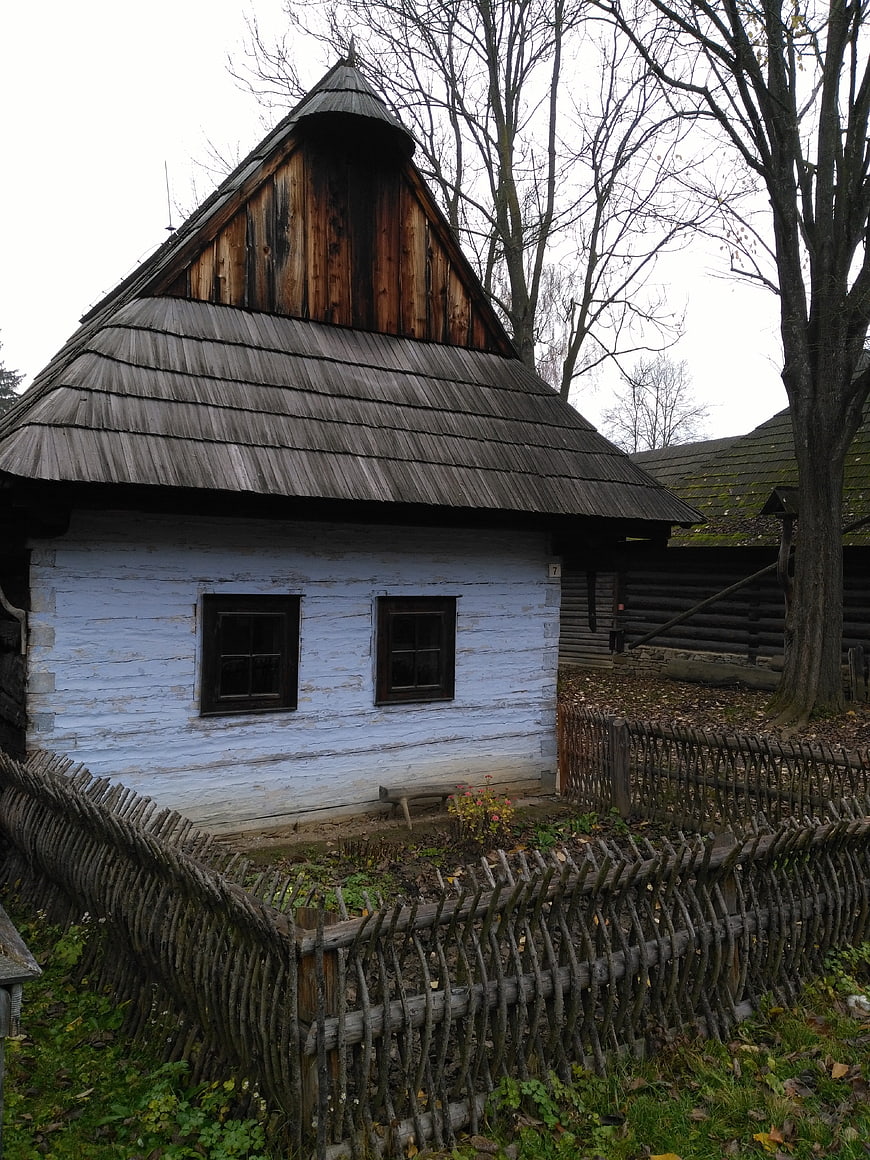 Traditional wooden house with shingle roof and wattle fence