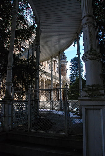 Ornate white gazebo with iron fence and historic villa background