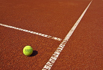 Yellow tennis ball on red clay court corner