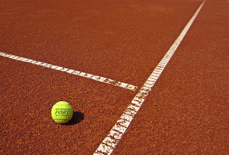 Yellow tennis ball on red clay court corner