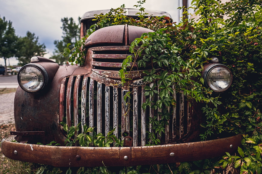 Rusty vintage car overgrown with green vines