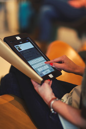 Close-up of woman typing on tablet with red nails
