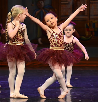 Young ballet dancers performing on stage in maroon and gold costumes