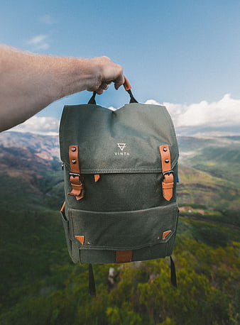 Green Canvas Backpack Held Against Mountain Landscape