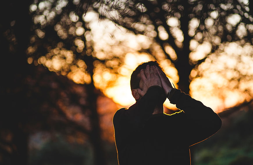 Silhouette of a distressed man holding his head at sunset