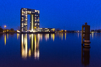 Modern square building with hole reflecting in water at blue hour