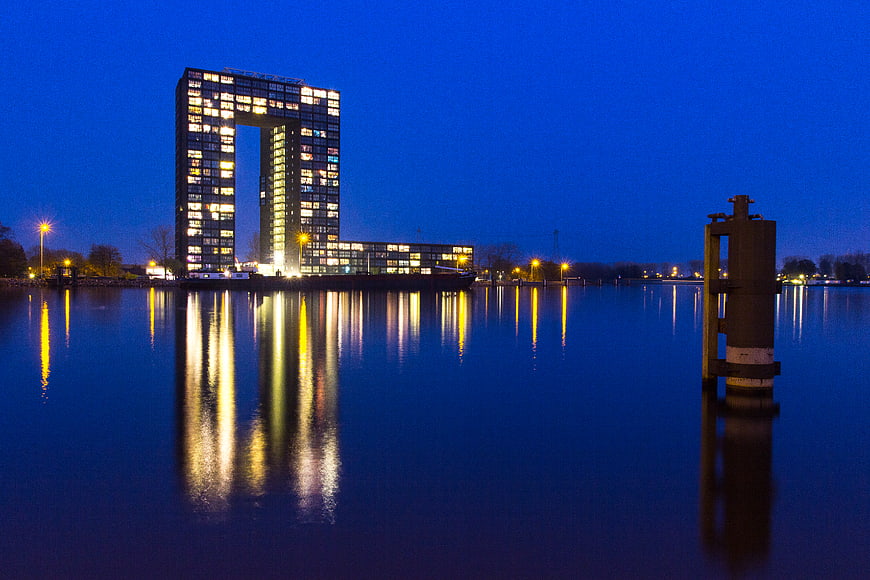 Modern square building with hole reflecting in water at blue hour