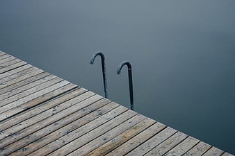 Minimalist wooden dock with metal ladder in calm water