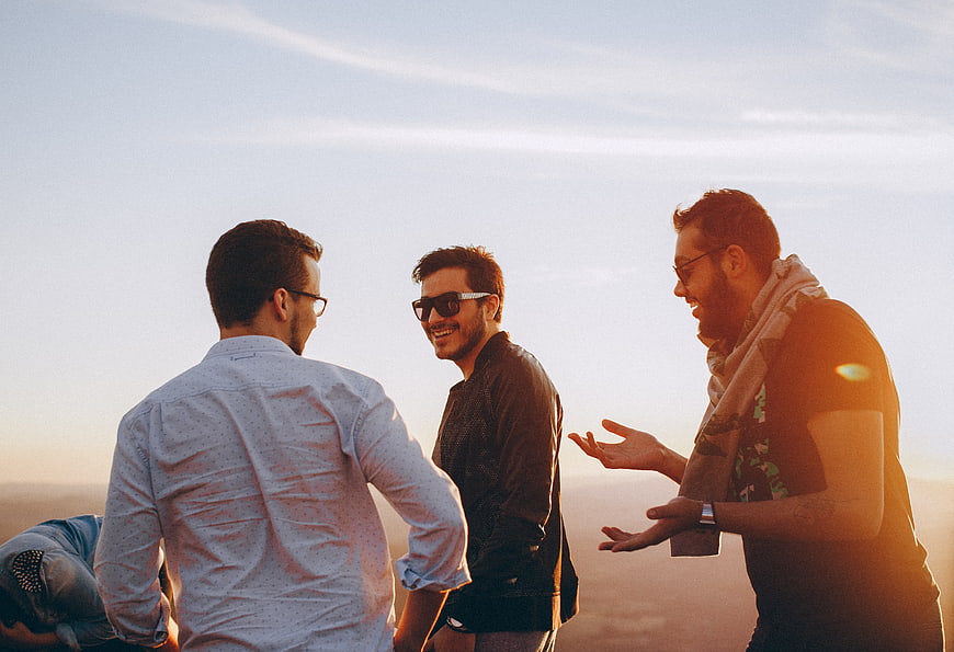 Three happy men laughing and talking on a mountain at sunset