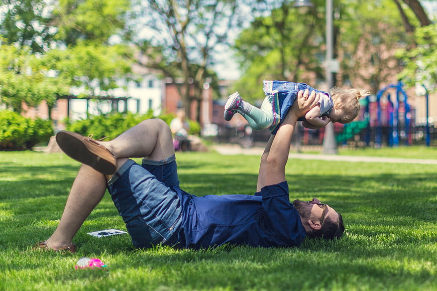 Father lifting baby in the air on grassy park lawn