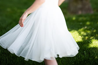 Woman in flowing white dress twirling on green grass