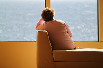 Senior woman sitting alone on sofa looking out window at water