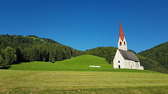 White Chapel with Red Spire in Green Alpine Meadow