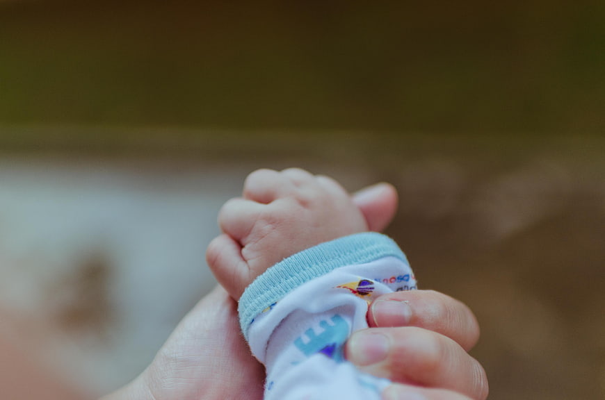 Close-up of adult hand holding baby's tiny hand