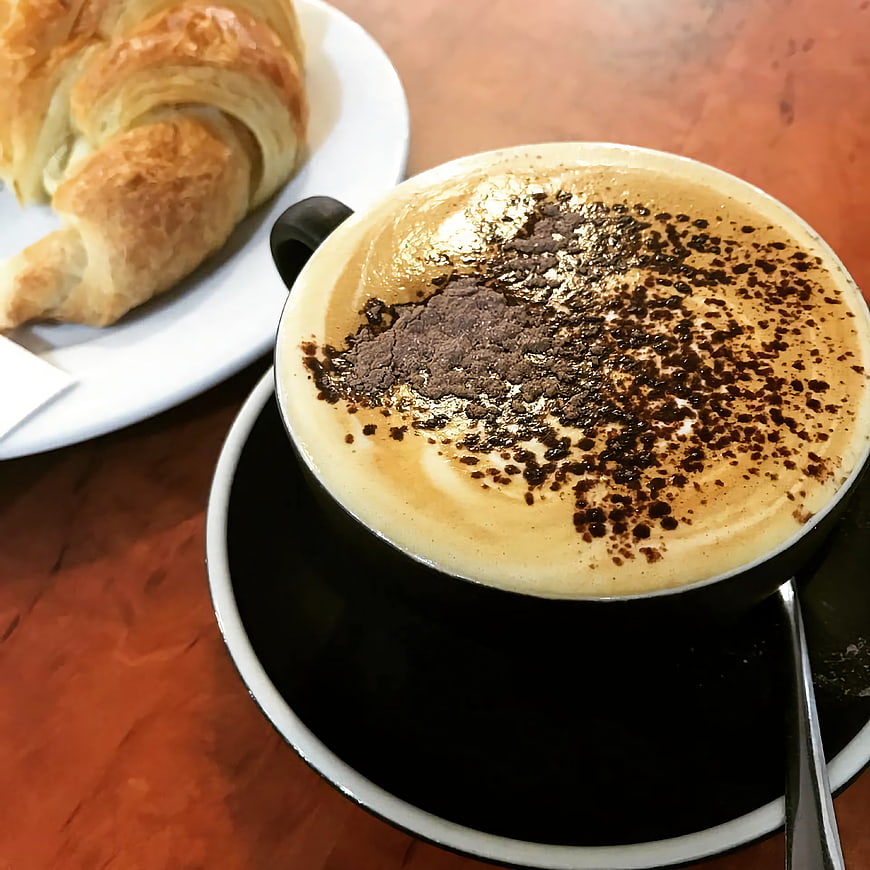 Cappuccino with Cocoa Powder and Croissant on Wooden Table