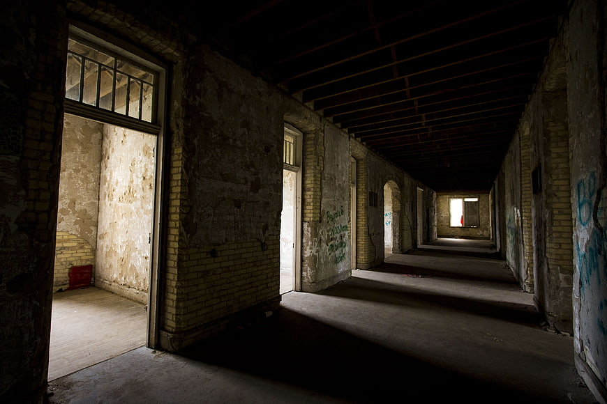 Dark abandoned hospital corridor with peeling paint and graffiti