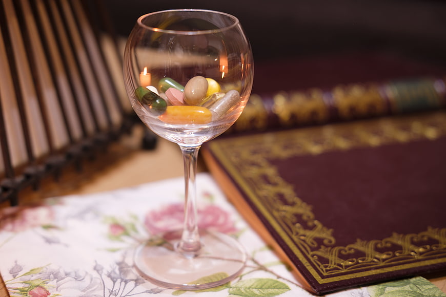 Pills in wine glass on floral cloth with vintage book