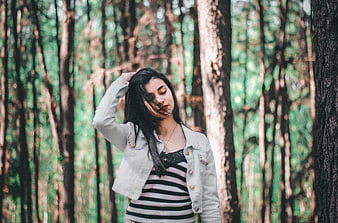 Young woman with dark hair in striped shirt and jacket in forest