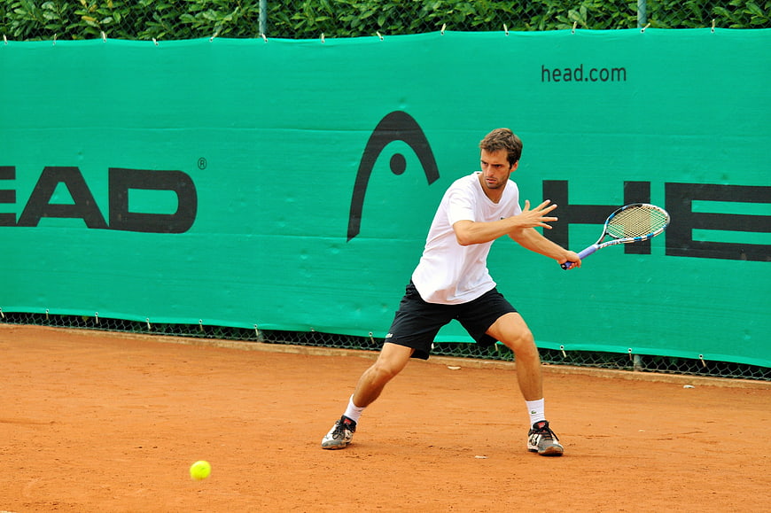 Male tennis player hitting a backhand on a clay court