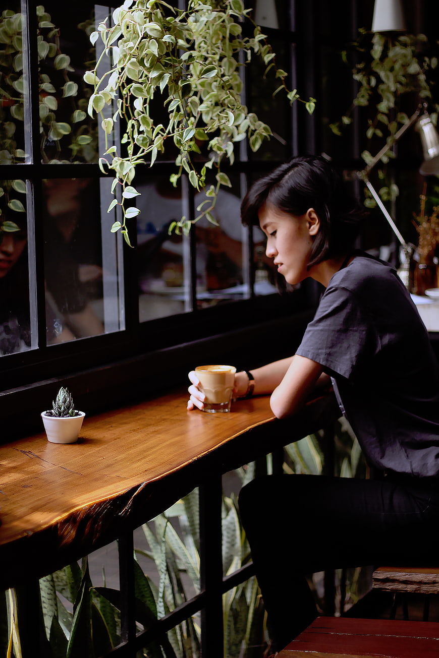 Woman drinking coffee at cafe window with plants