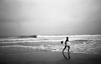 Surfer walking on beach with board in black and white