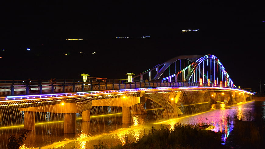 Colorful illuminated bridge with water curtain at night