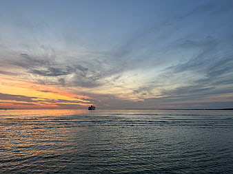 Serene Sunset Over Calm Ocean with Distant Ship Silhouette