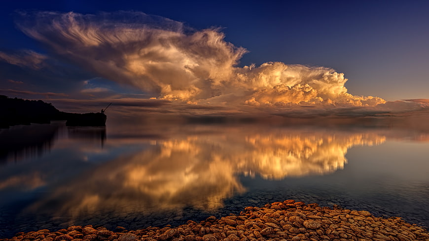 Dramatic sunset clouds reflecting on calm water with rocky shore