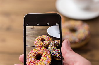 Hand holding smartphone photographing colorful sprinkled donuts