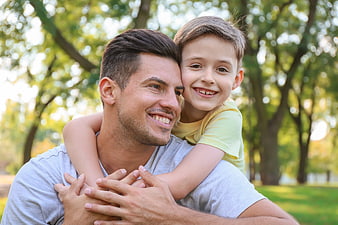 Happy father carrying smiling son on back in park