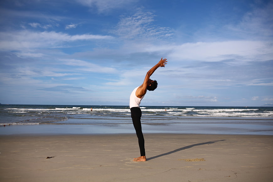 Woman performing standing yoga pose on a sandy beach