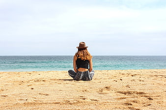 Woman in Hat Sitting on Sandy Beach Facing Ocean