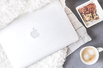 Flat lay of white laptop, coffee, and snacks on cozy blanket