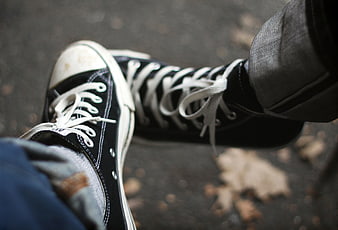 Close-up of black high-top sneakers on asphalt with autumn leaves