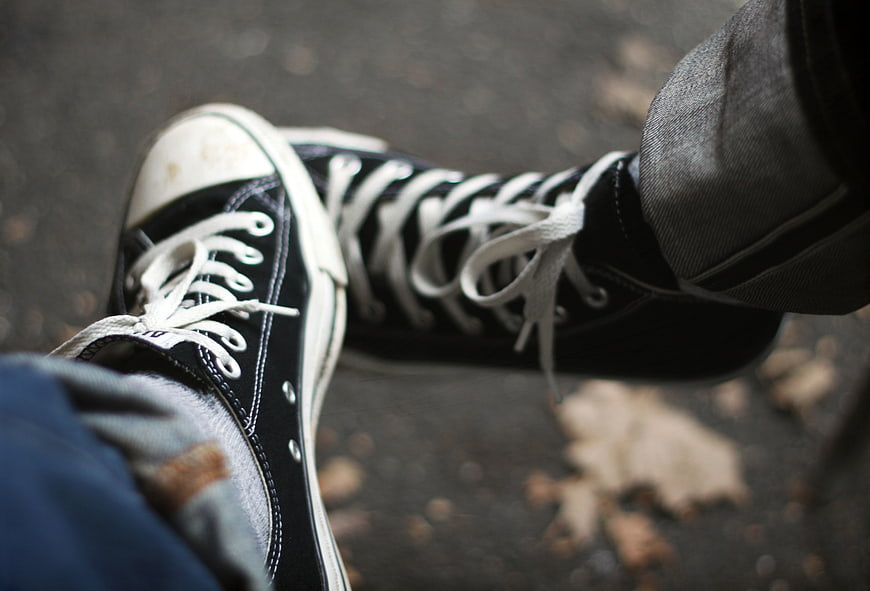 Close-up of black high-top sneakers on asphalt with autumn leaves