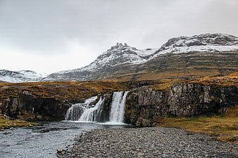 Scenic waterfall cascading into river with snow-capped mountains
