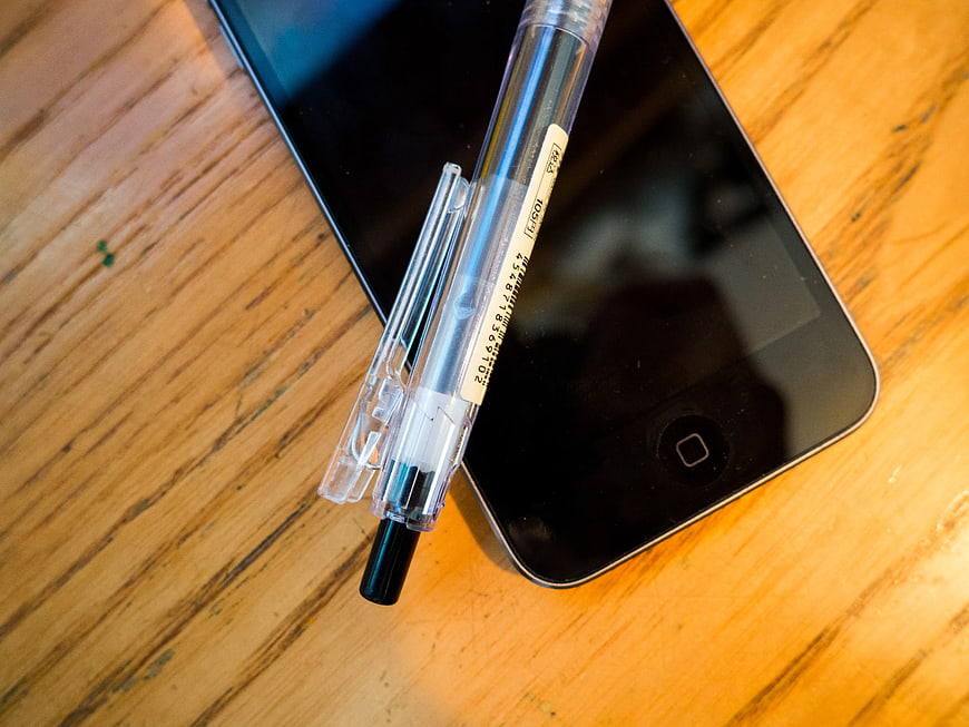 Clear Ballpoint Pen on Black Smartphone on Wooden Desk