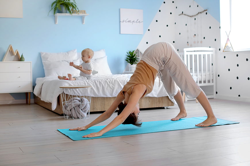 Mother doing yoga in bedroom with toddler playing on bed