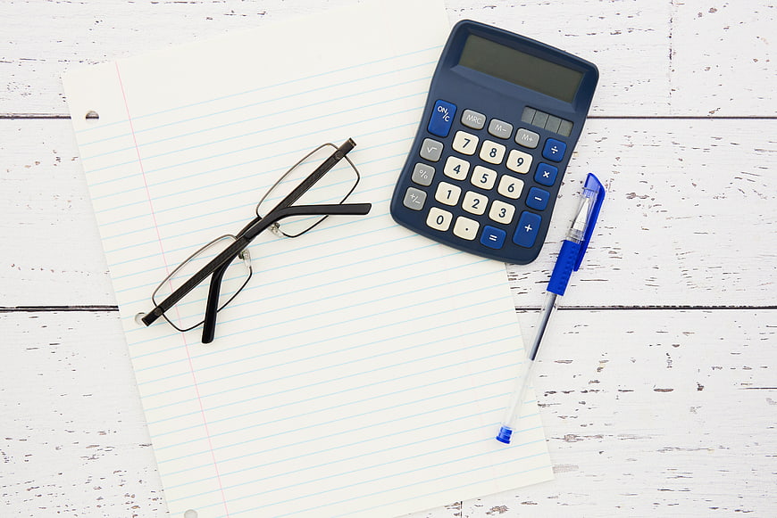 Flat lay of calculator, glasses, and pen on notebook