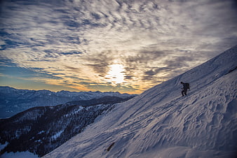 Backcountry skier ascending snowy mountain slope at sunset