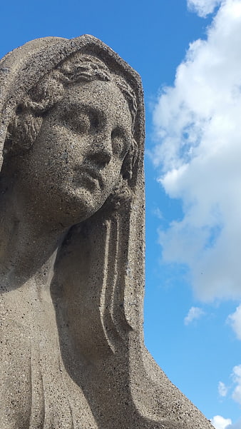 Close-up of weathered stone statue head against blue sky