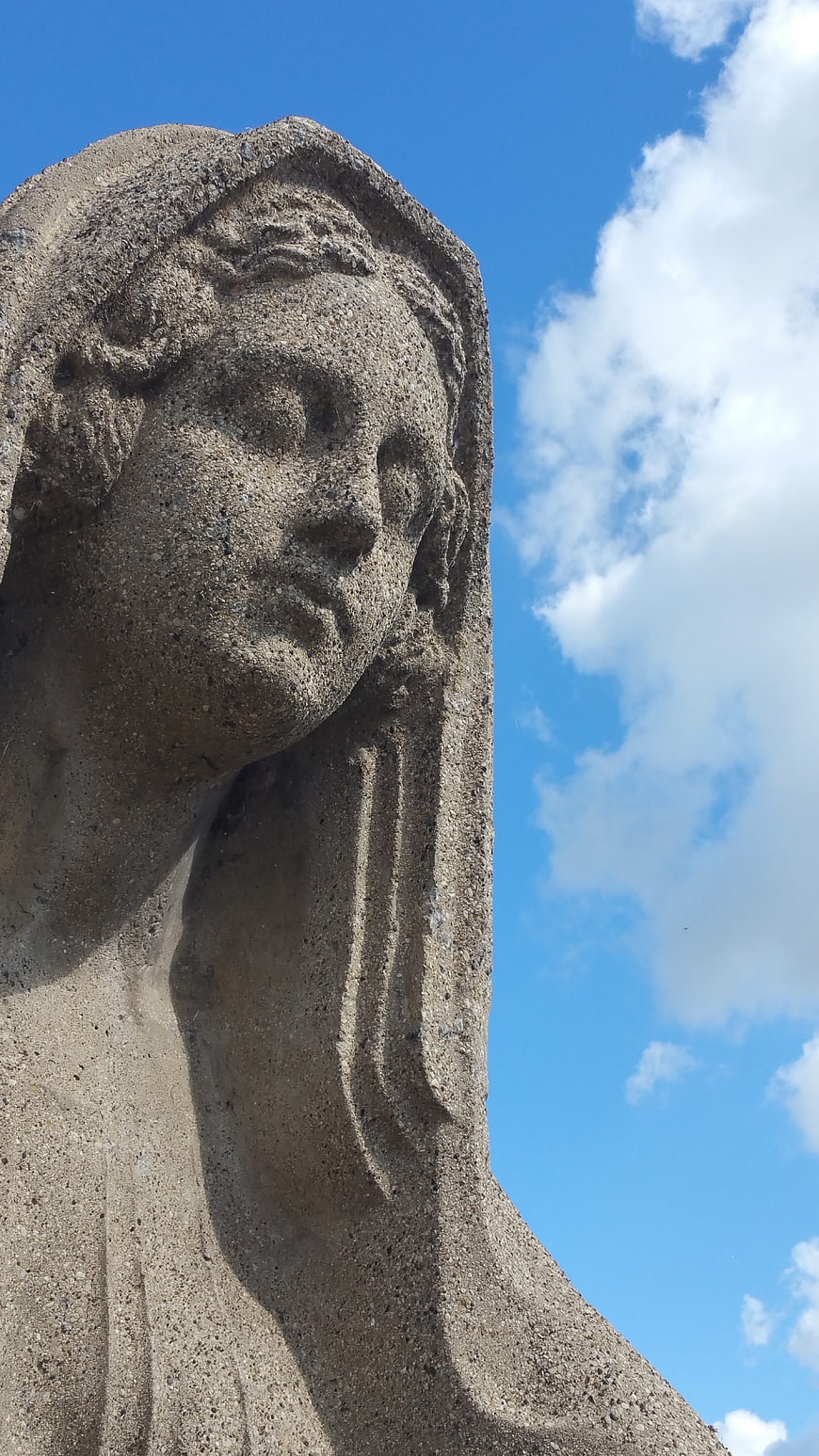 Close-up of weathered stone statue head against blue sky