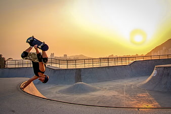 Skateboarder performing handstand trick at sunset skatepark