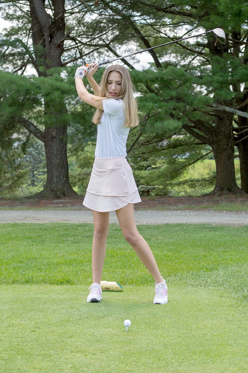 Young woman golfer swinging club on green course