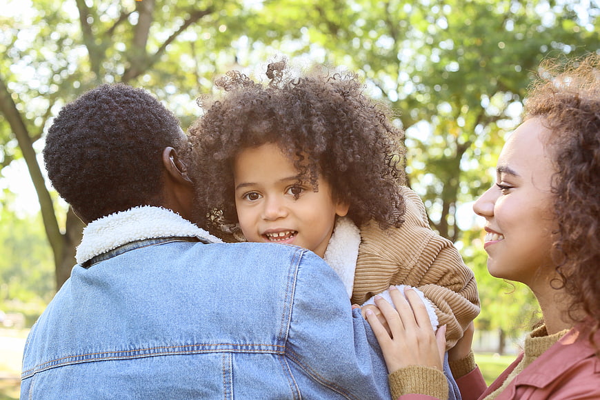 Happy African American family hugging in a sunny park