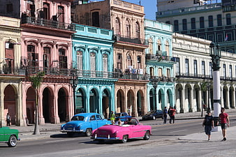 Vintage cars driving past colorful colonial buildings in Havana