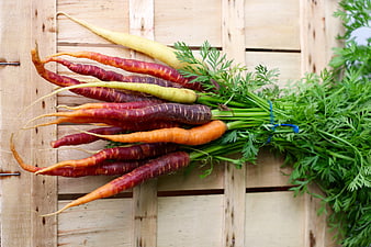 Assorted heirloom carrots with green tops on rustic wooden crate
