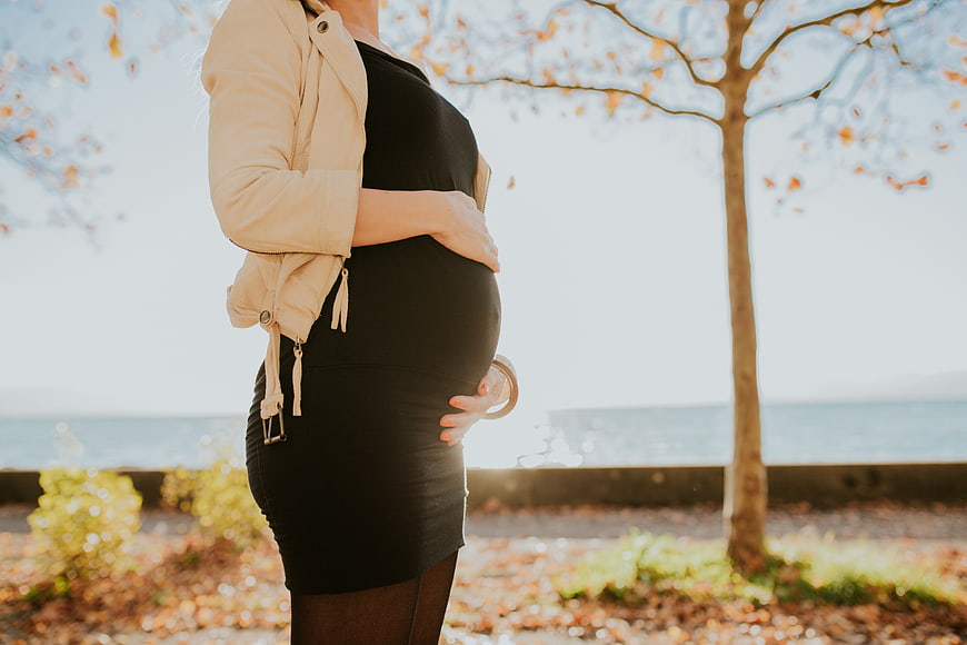 Pregnant woman holding belly outdoors in autumn