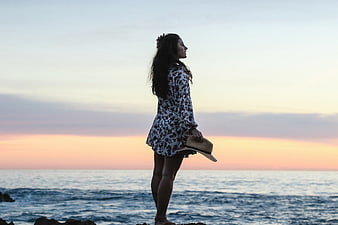 Woman in Floral Dress Standing by Ocean at Sunset