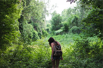 Young woman with backpack hiking through lush green forest